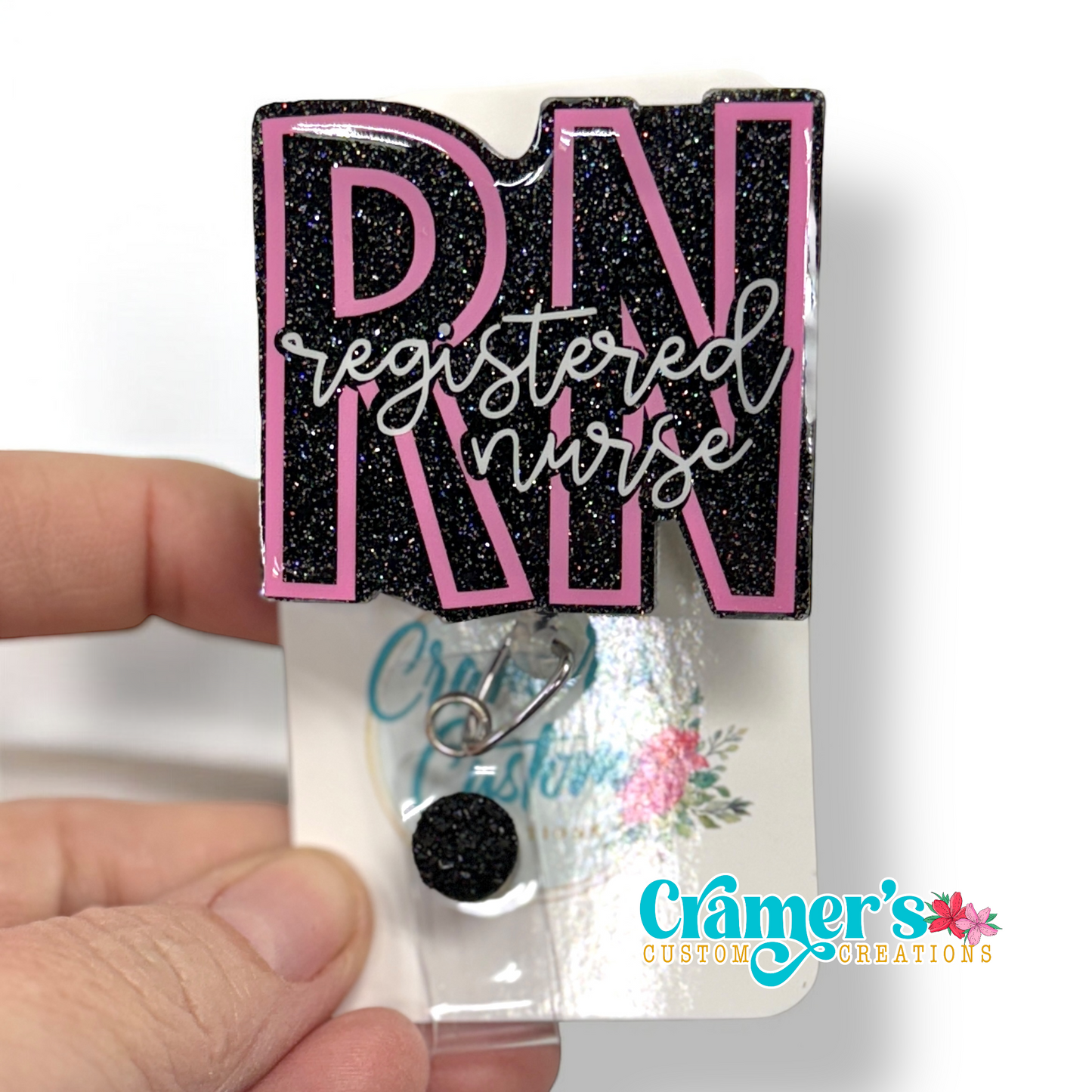 badge reel showing a black glitter background with the initials in pink and registered nurse in white