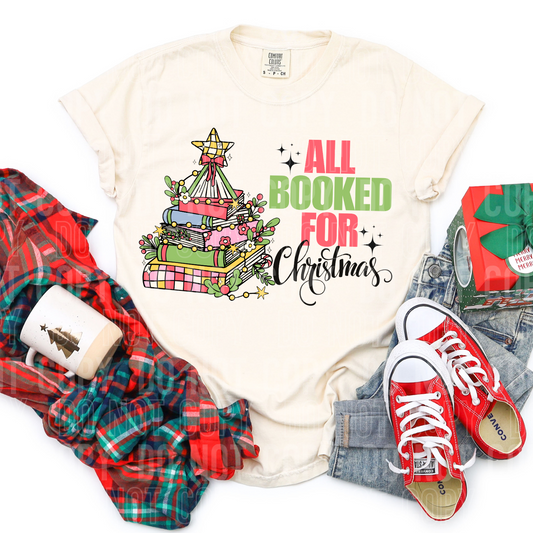 showing a shirt surrounded by clothing and a stack of books in the shape of a christmas tree saying all booked for christmas