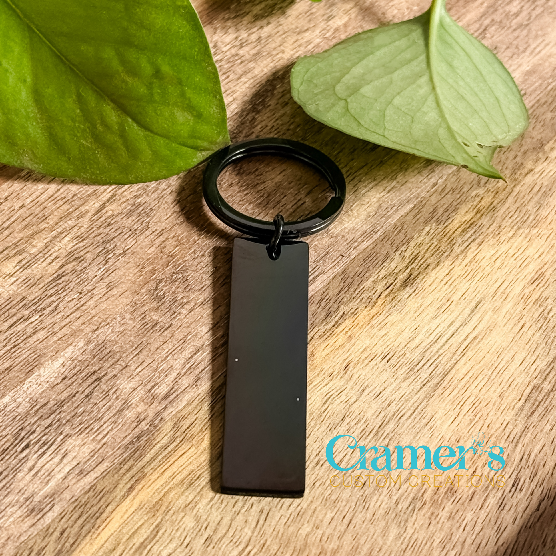 A black rectangle keychain with a keyring on one end and a leaf in the background.