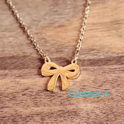 Gold bow-shaped pendant necklace on a wooden surface with 'Cramer's Custom Creations' branding.