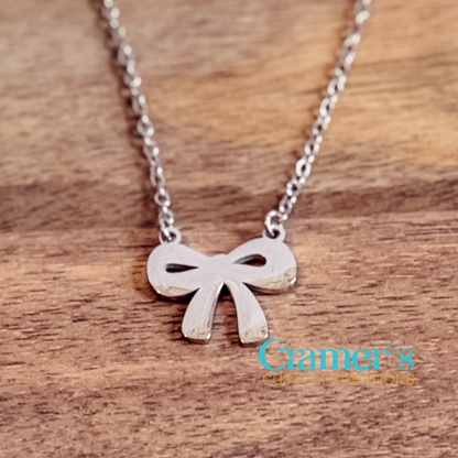 Silver bow necklace on a wooden surface with 'Cramer's Custom Creations' logo.
