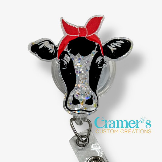 Cow-shaped badge holder with a red bow and glittery design, featuring Cramer's Custom Creations logo.