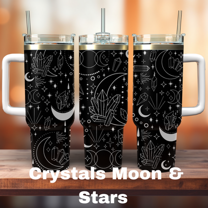 Three 40 oz tumblers with a black background, featuring laser engraved designs of crystals, moons, and stars. One tumbler has a straw, and the design is spread across the surface of both tumblers.