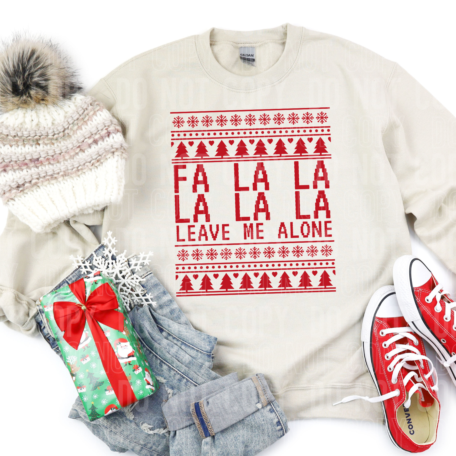 A sweatshirt  that says fa la la la la leave me alone  in christmas sweater style  surrounded by clothes and a gift 