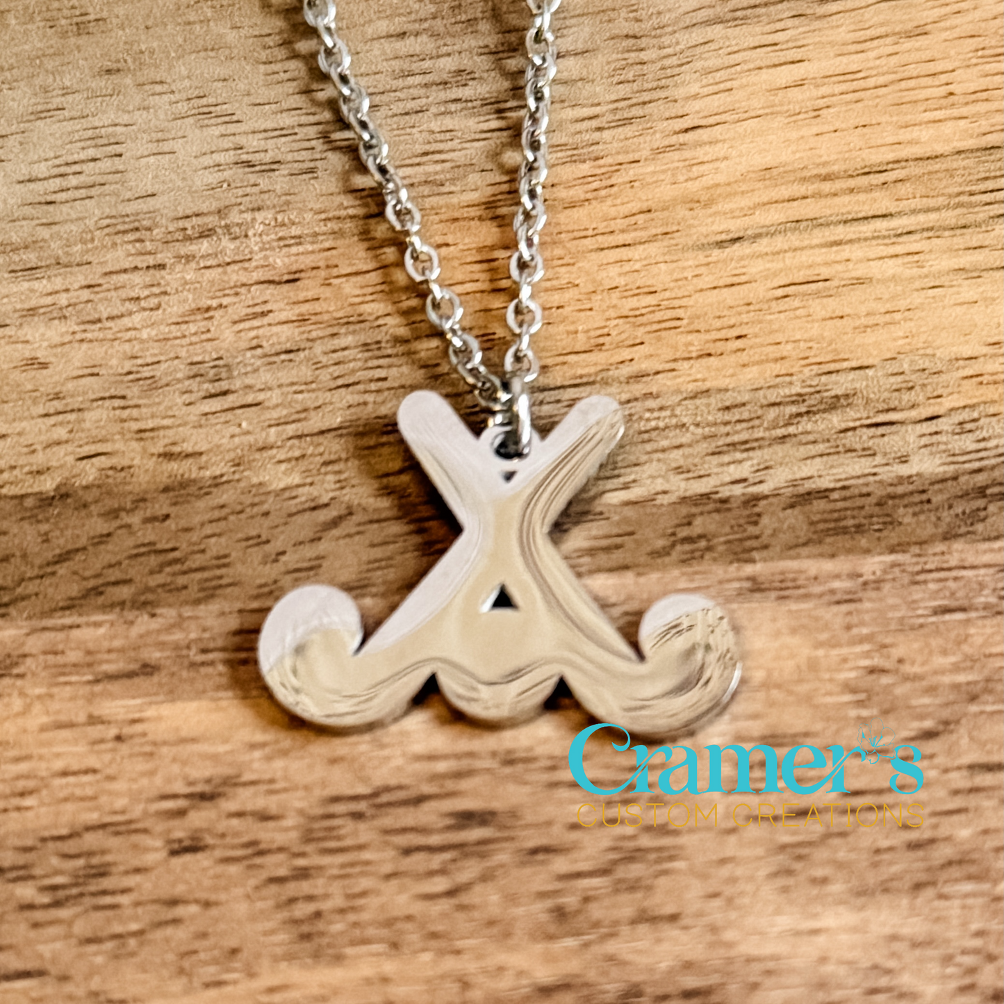 Silver field hockey  pendant on a wooden surface, featuring Clamer's Custom Creations logo.