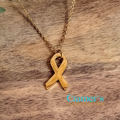 Gold ribbon necklace on a wooden surface with 'Cramer's Custom Creations' logo.