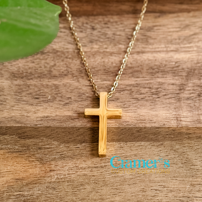 Gold cross necklace on a wooden surface with 'Cramer's' logo.