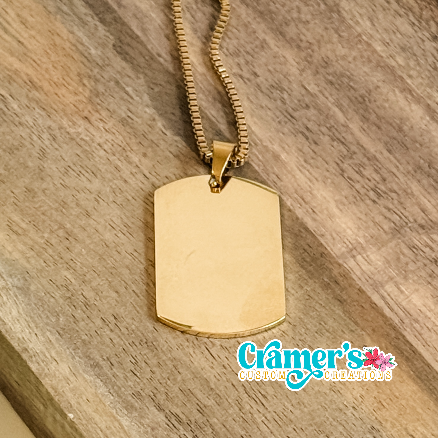 Gold dog tag necklace on a wooden surface with 'Cramer's Custom Creations' branding.