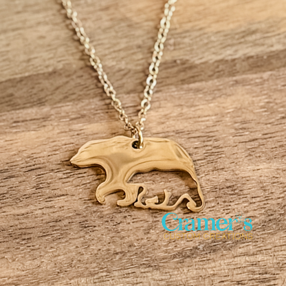 Gold necklace with a bear pendant on a wooden surface, featuring Cramer's Custom Creations logo.