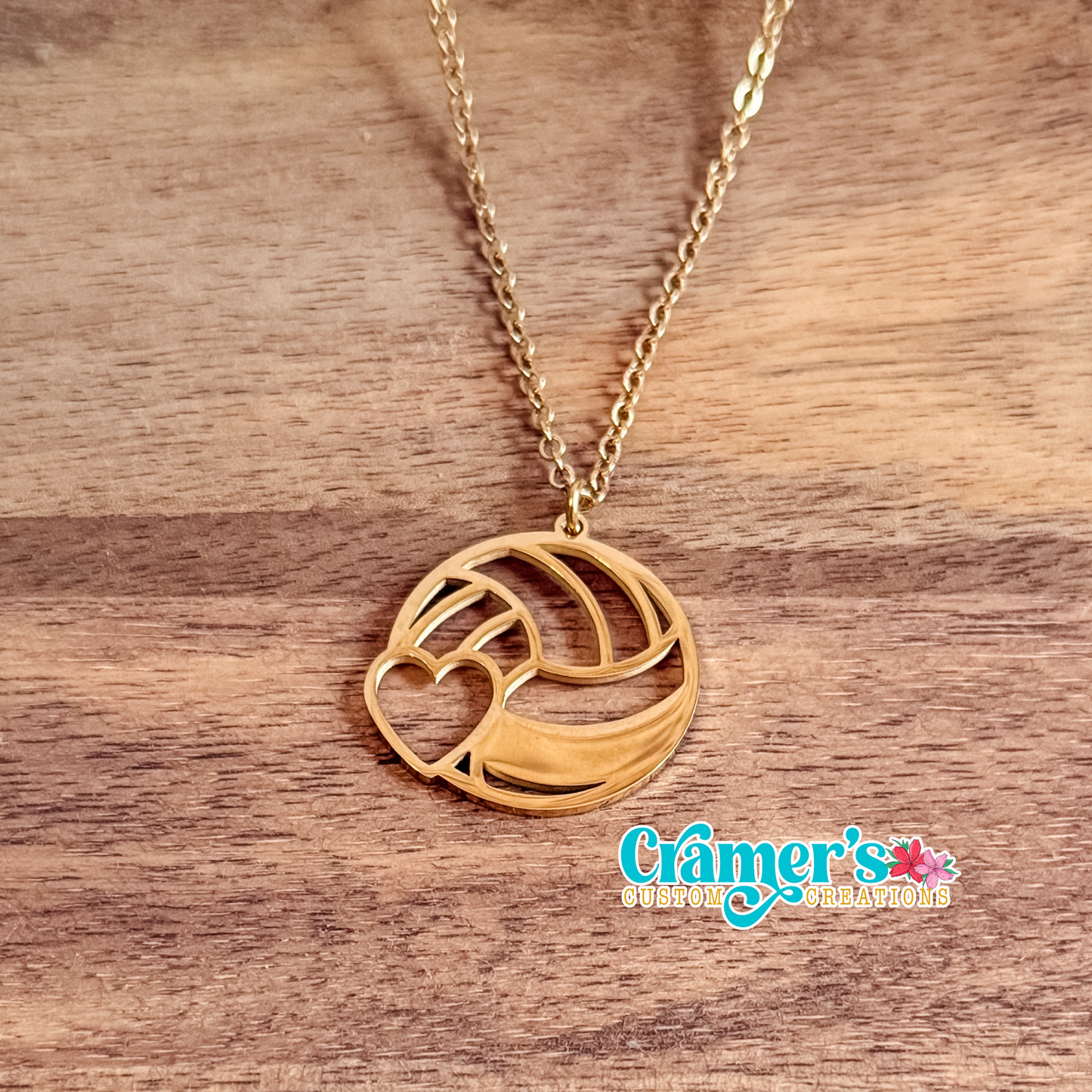 Gold necklace with a volleyball pendant on a wooden surface, featuring the 'Cramer's Custom Creations' logo.