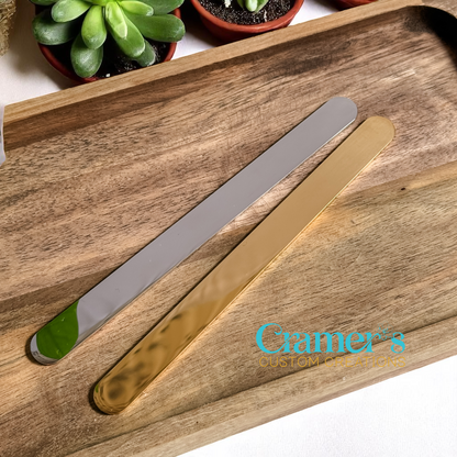 Two metal flat bracelets on a wooden tray with 'Cramer's Creations' branding.