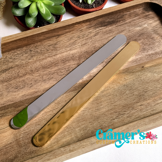 Two metal flat bracelets on a wooden tray with 'Cramer's Creations' branding.