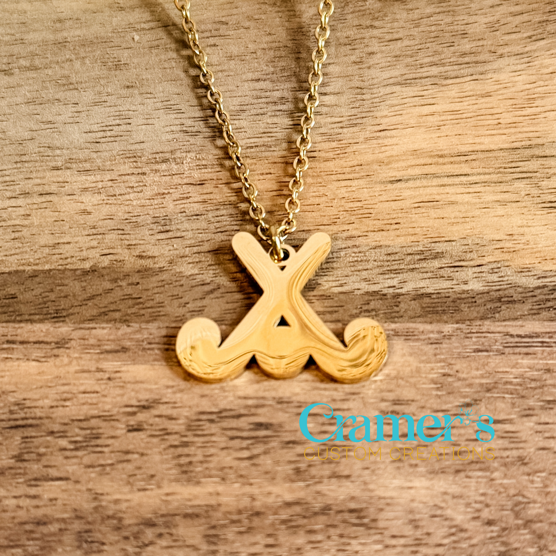 Gold necklace with a field hockey pendant on a wooden surface, featuring the Cramer's Custom Creations logo.