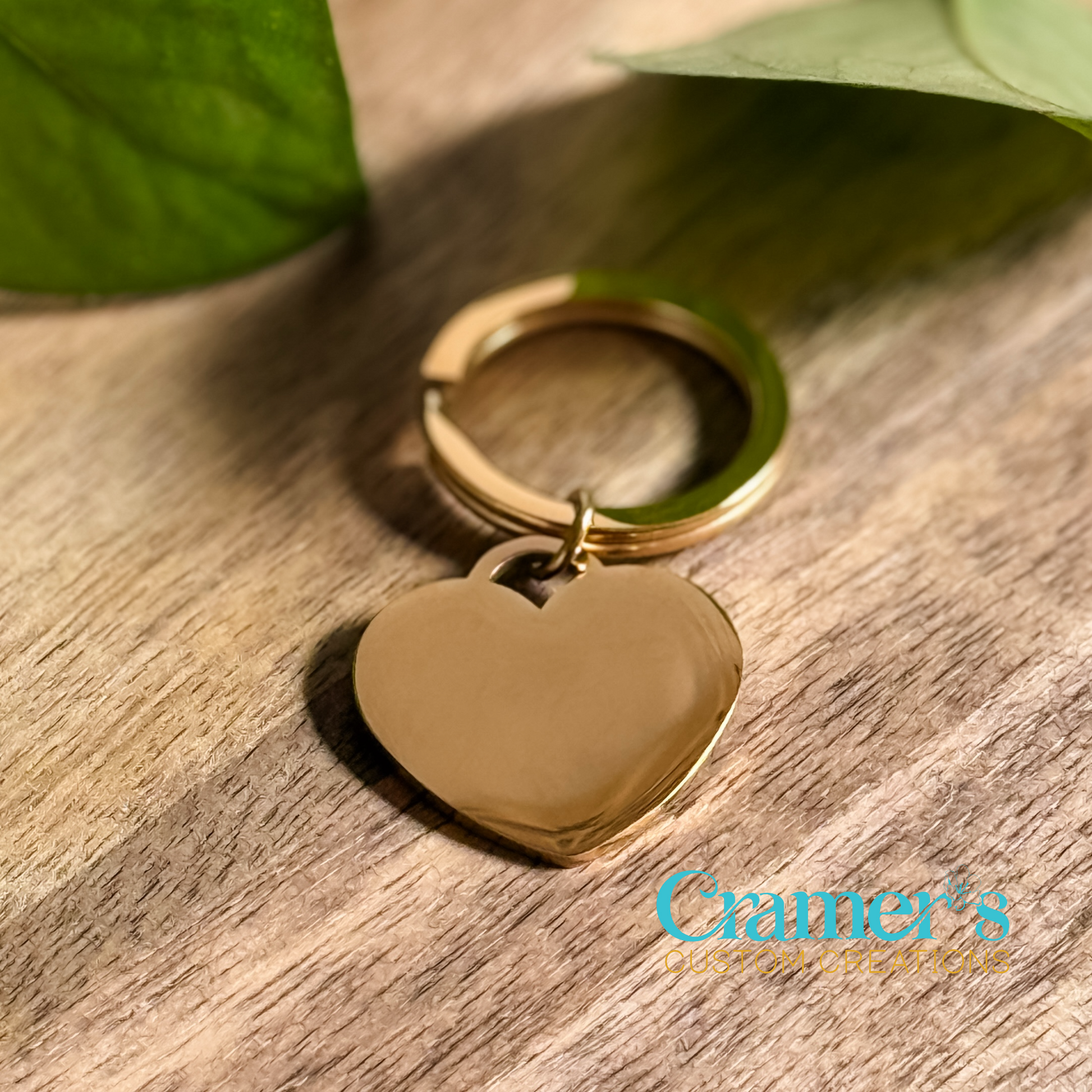 A gold-colored heart-shaped keychain on a wooden surface, with a leaf in the background.