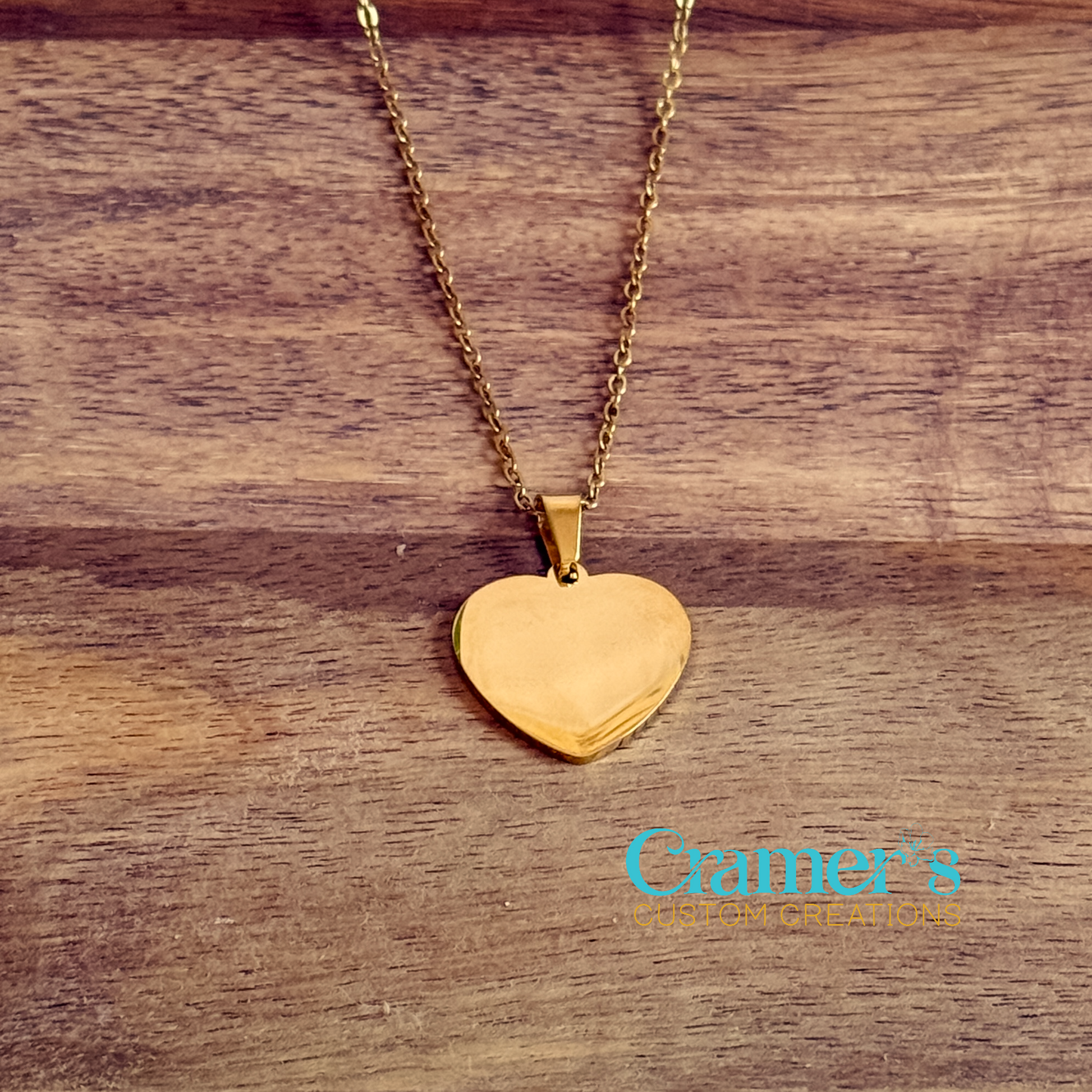 Gold heart-shaped pendant necklace on a wooden surface with 'Cramer's Custom Creations' branding.