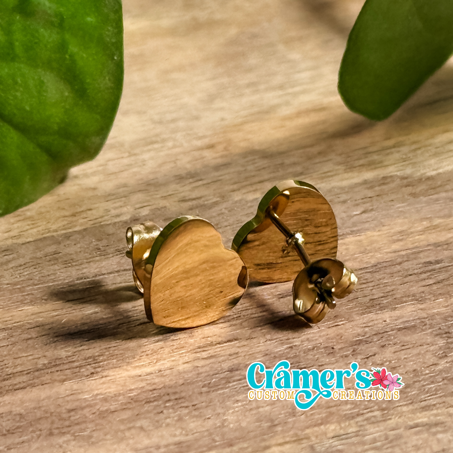a pair of gold heart stud earrings on a wood background