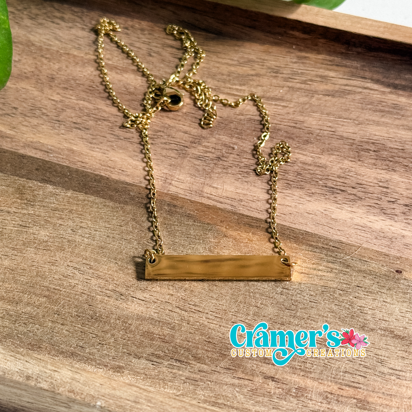 Gold necklace on a wooden surface with 'Cramer's Custom Creations' branding.
