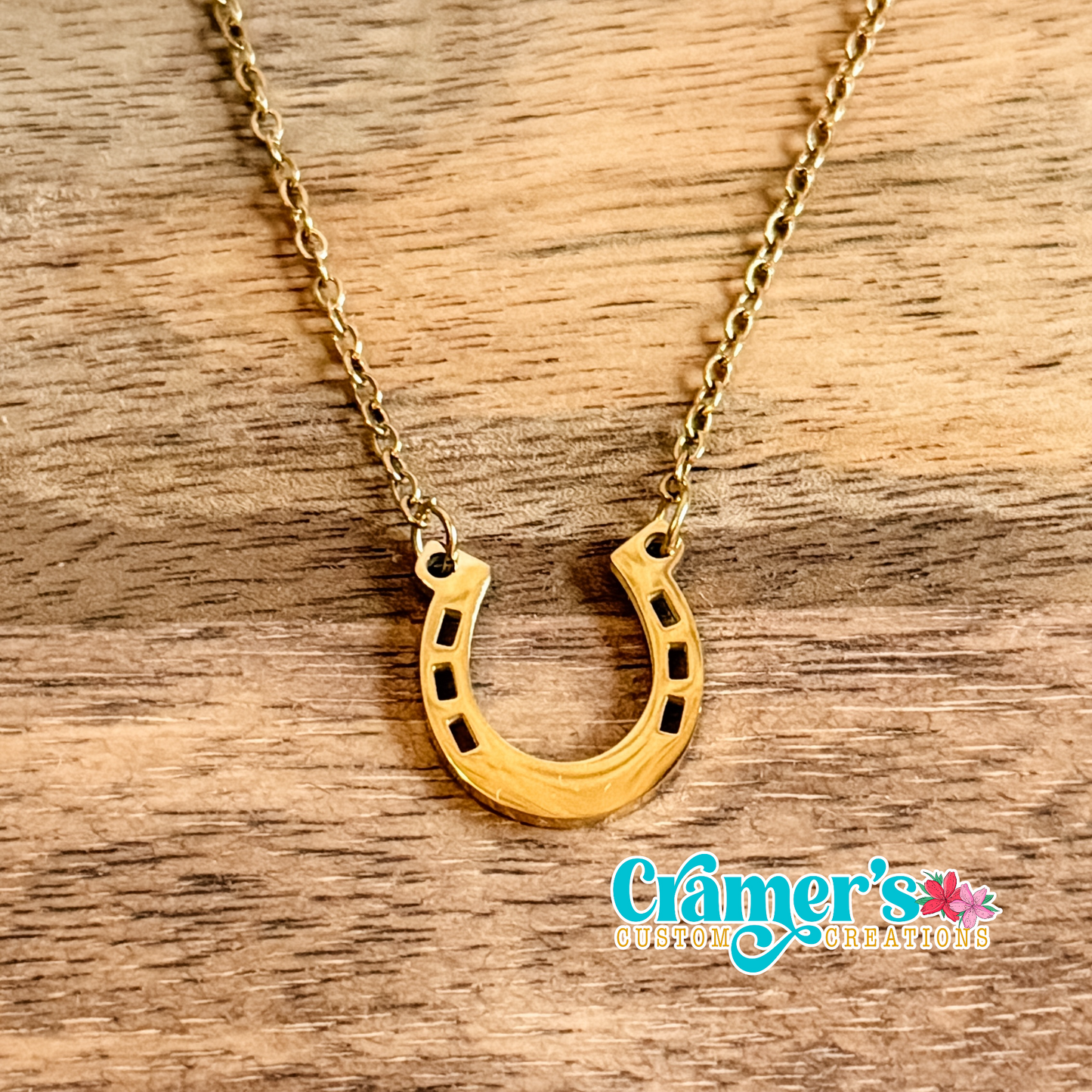 Gold horseshoe necklace on a wooden surface with 'Cramer's' branding.