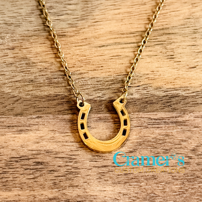 Gold horseshoe necklace on a wooden surface with 'Cramer's' branding.