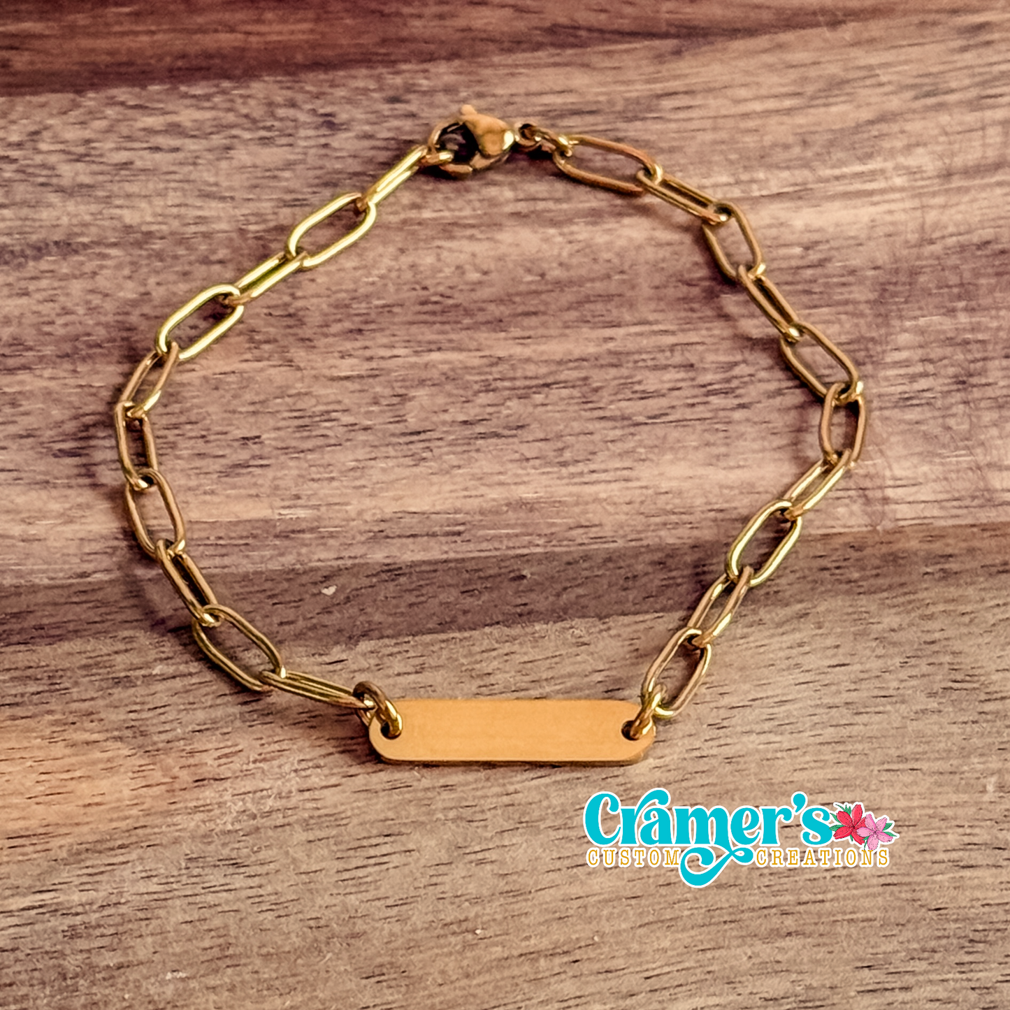 Gold chain bracelet on a wooden surface with 'Cramer's Custom Creations' branding.