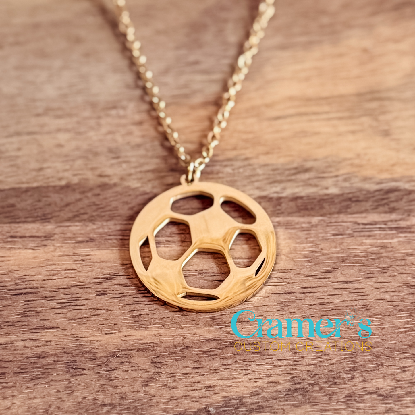 Gold soccer ball necklace on a wooden surface with 'Cramer's Custom Creations' logo.