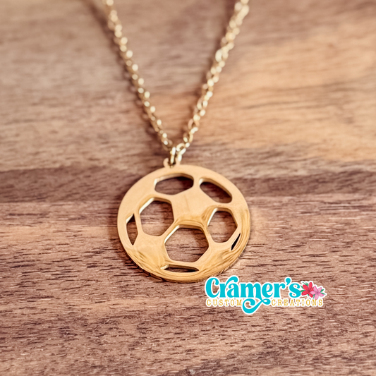 Gold soccer ball necklace on a wooden surface with 'Cramer's Custom Creations' logo.