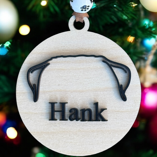 an plain wood ornament with only an ear outline and a name in black in front of a christmas tree