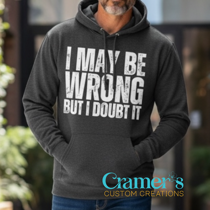Person wearing a hoodie with 'I May Be Wrong But I Doubt It' text, outdoors.