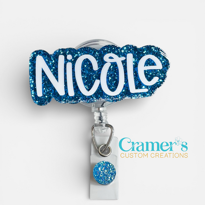 Blue glittery badge holder with 'Nicole' text on a white background, featuring Cramer's Custom Creations logo.