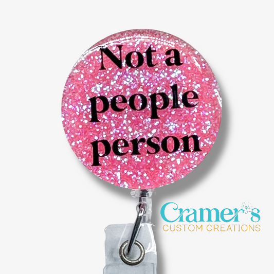 Pink glittery badge holder with 'Not a people person' text and Cramer's Custom Creations logo.