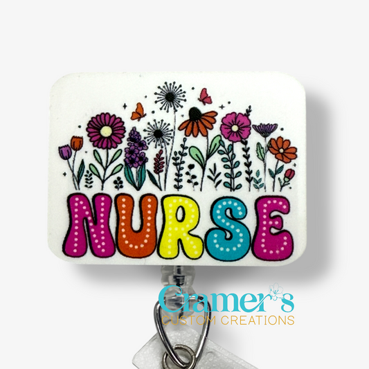 Colorful 'NURSE' badge topper with flowers on a white background, featuring Cramer's Custom Creations logo.