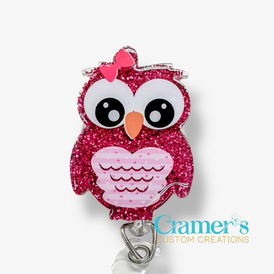 Pink glittery owl-shaped badge holder with a pink bow on a white background, featuring the brand 'Cramer's Custom Creations'.
