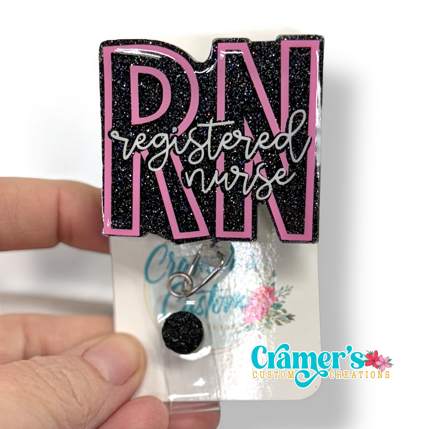 badge reel showing a black glitter background with the initials in pink and registered nurse in white 