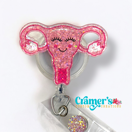 pink glittery uterus badge reel with a smile on its face