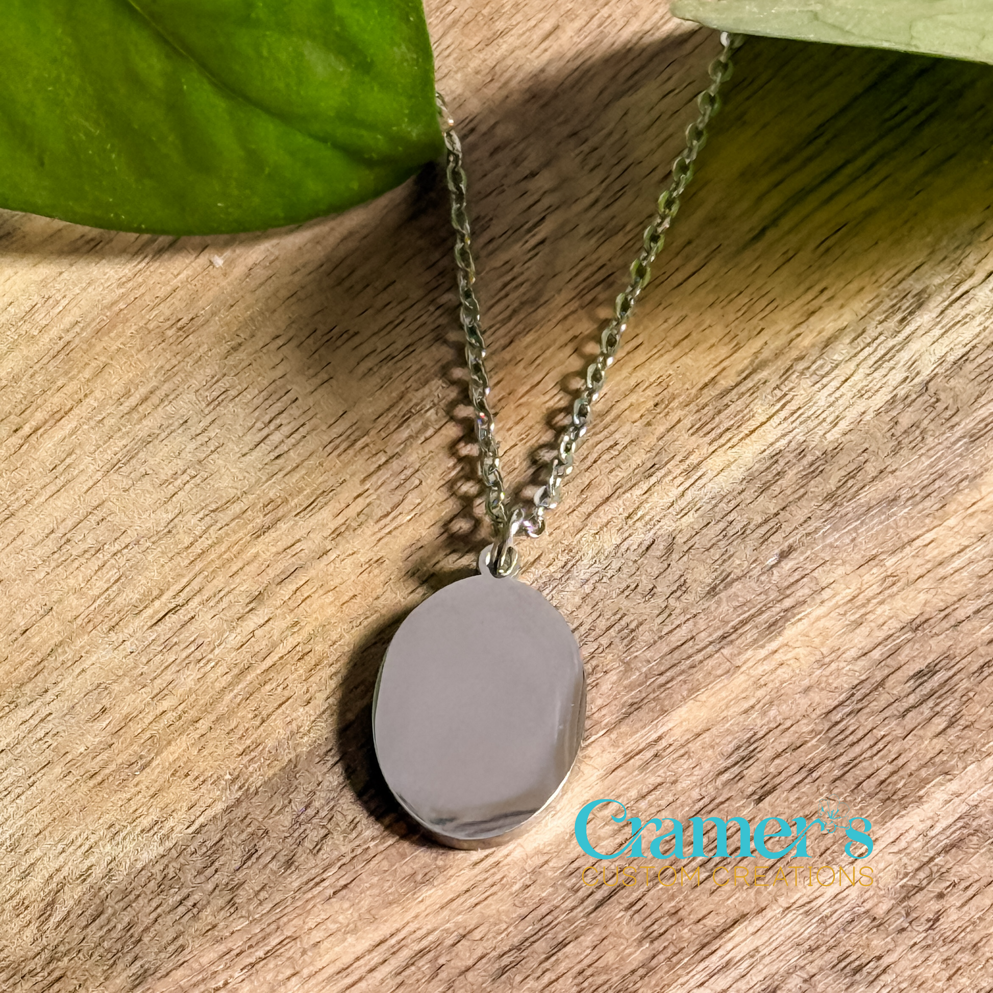a silver oval pendant necklace on a wood backgroundd