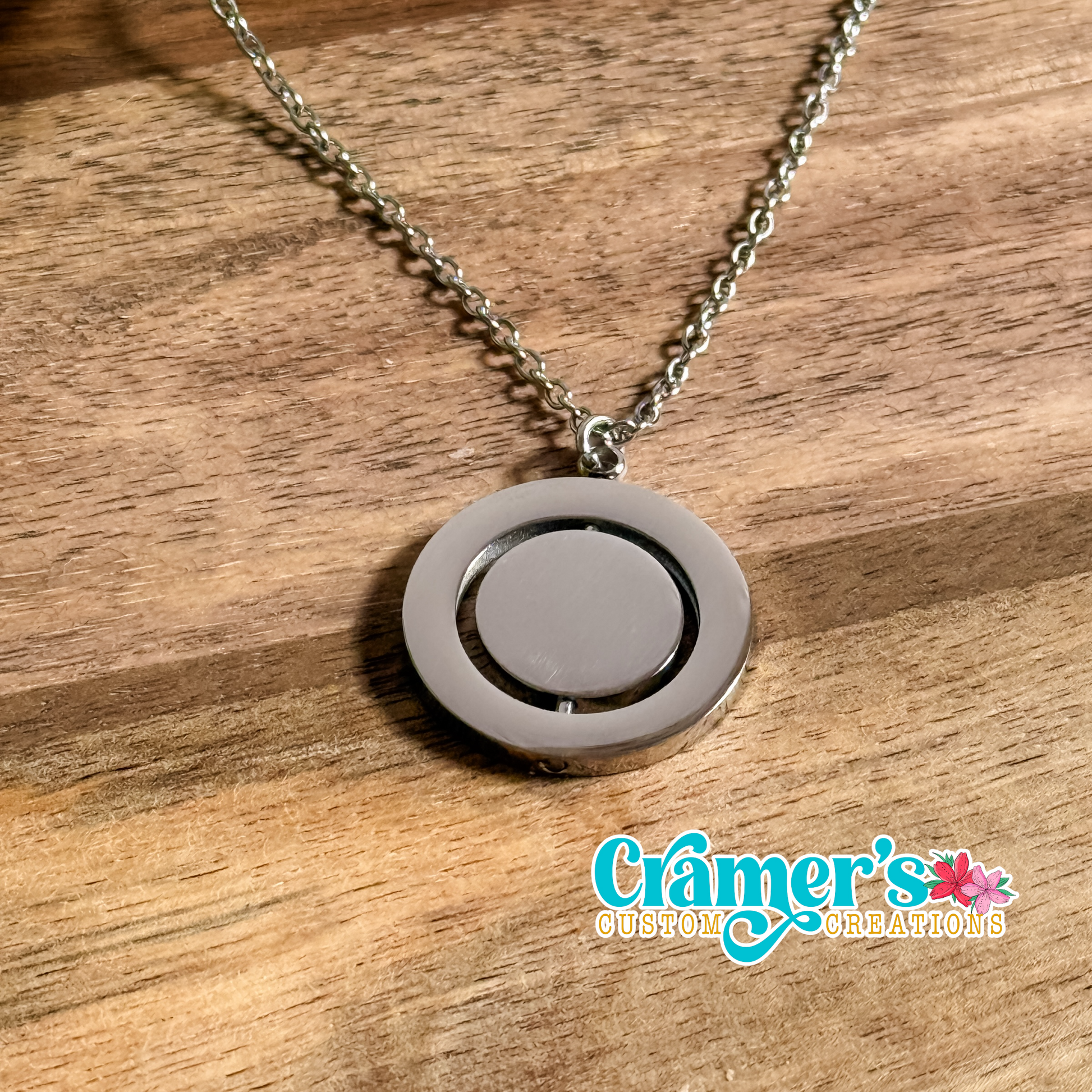 A rotating circle pendant necklace with a silver chain, displayed on a wooden surface. The necklace features a design with a larger outer circle and a smaller inner circle that rotates.