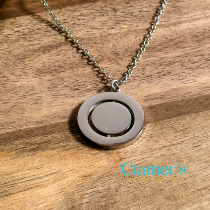 A rotating circle pendant necklace with a silver chain, displayed on a wooden surface. The necklace features a design with a larger outer circle and a smaller inner circle that rotates.