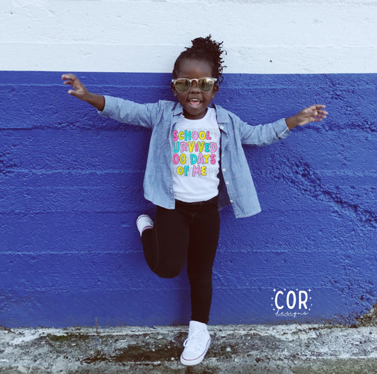 little girl standing against a wall wearing a tshirt that says school survived100 days of me