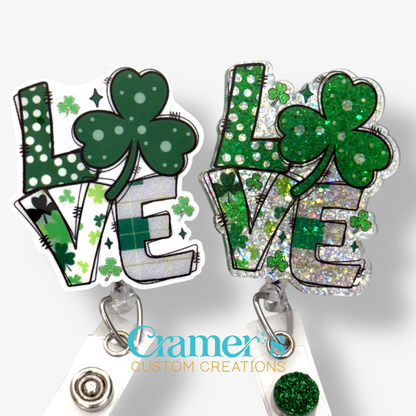 2 badge reels showing a glitter and a non glitter option of a badge with the word love with a shamrock being the O