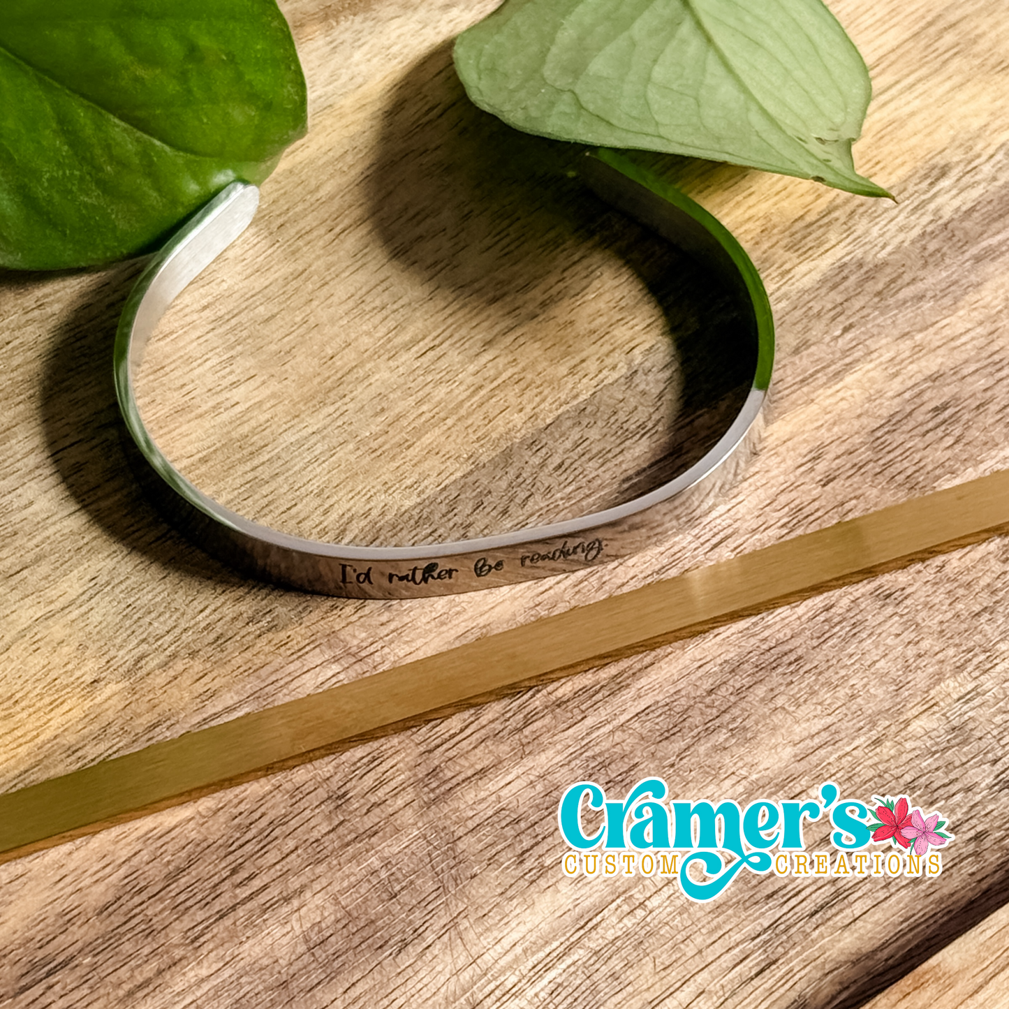 a silver bangle bracelet with writing on it, laying next to a gold blank one, on a wood background