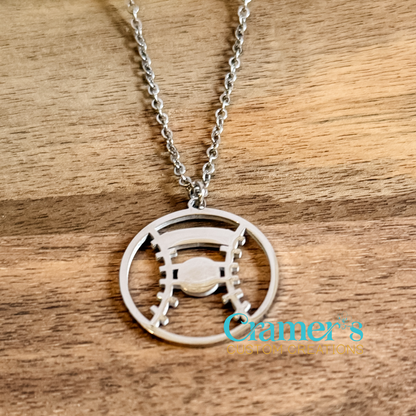 Silver necklace with a baseball or softball  pendant on a wooden surface, featuring the Cramer's Custom Jewelry logo.