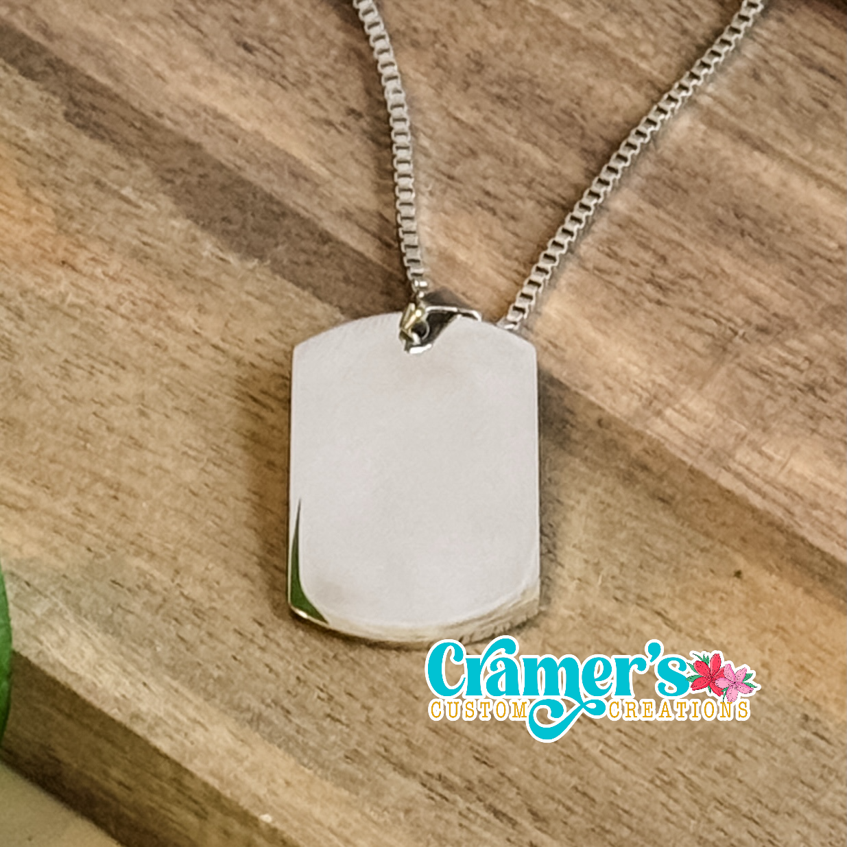 Silver dog tag necklace on a wooden surface with 'Cramer's Custom Creations' logo.