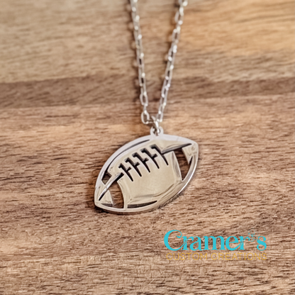 Silver football-shaped pendant necklace on a wooden surface with 'Gramer's Custom Creations' branding.