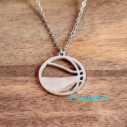 Silver necklace with a basketball pendant on a wooden surface, featuring 'Cramer's Custom Creations' logo.