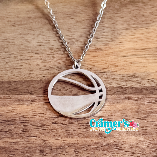 Silver necklace with a basketball pendant on a wooden surface, featuring 'Cramer's Custom Creations' logo.