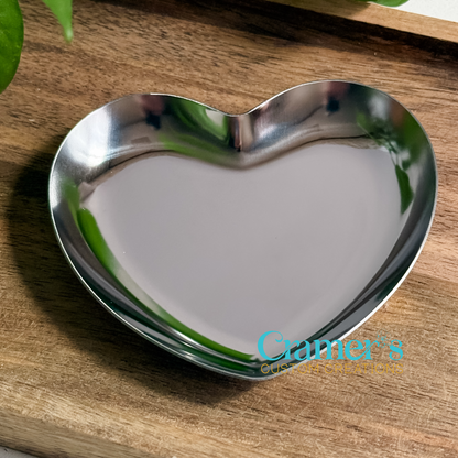 Heart-shaped metal ring dish on a wooden surface with 'Cramer's' branding.