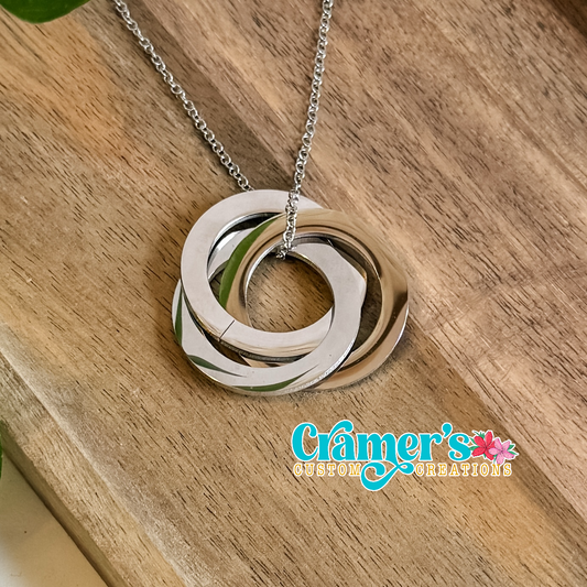 Necklace with interlocking rings on a wooden surface, featuring Cramer's Custom Creations logo.