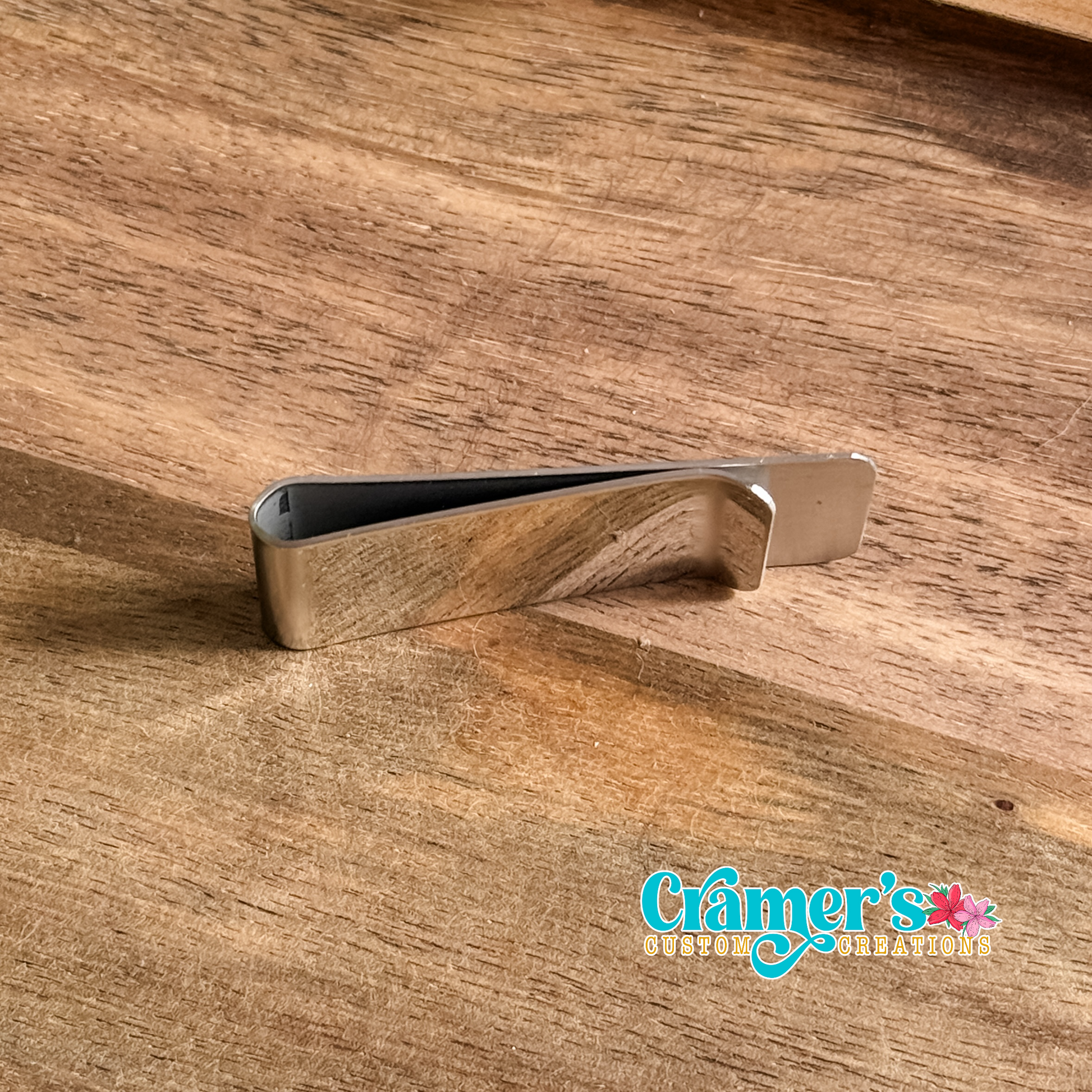 Silver money clip on a wooden surface with 'Cramer's Custom Creations' branding.