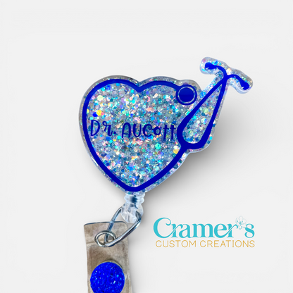 Heart-shaped badge reel with blue glittery design and 'Dr. Nicole' text, featuring Cramer's Custom Creations logo.