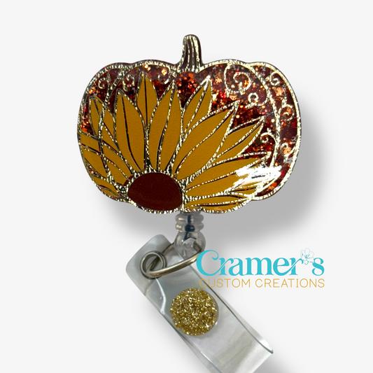 a pumpkin badge reel decorated with a sunflower and a gold filigree